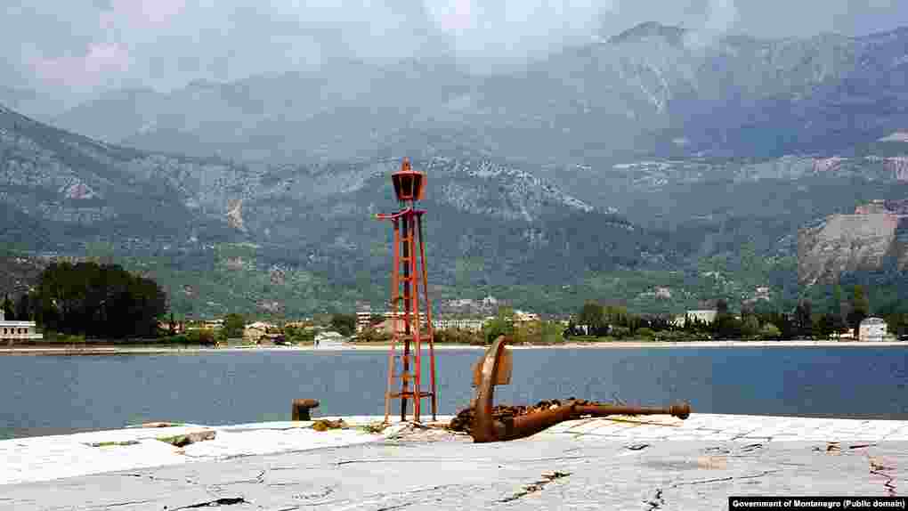Pogled sa svjetionika Pizane, dijela budvanskog pristaništa do kojeg je 1979. vodila od potresa napukla riva. Pogled na  zaleđe Slovenske plaže "ukrašavaju" betonski mastodonti, na samoj "pjeni od mora".  
