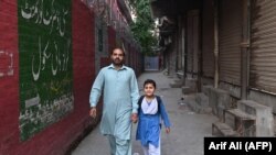 Лоҳур, дари бастаи мактабе дар пасманзари падару писаре. Акс аз соли 2023