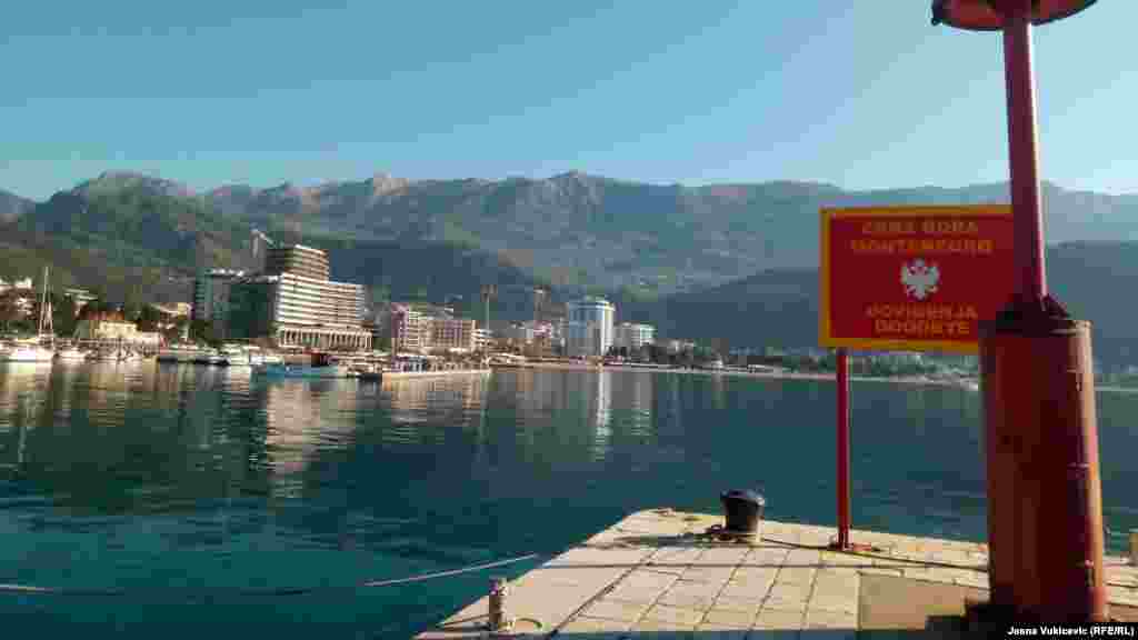 Pogled sa svjetionika Pizane, dijela budvanskog pristaništa do kojeg je 1979. vodila od potresa napukla riva. Pogled na  zaleđe Slovenske plaže "ukrašavaju" betonski mastodonti, na samoj "pjeni od mora".  