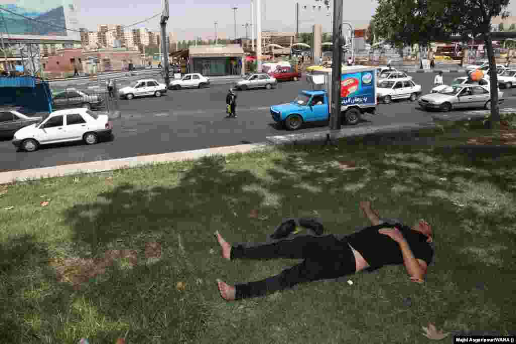 A man rests in the shade near a busy road in Tehran. The Health Ministry also warned that the two-day shutdown may need to be extended to protect people’s health.