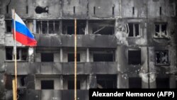 Російський прапор на тлі вигорілого – внаслідок бомбардувань і обстрілів російської армії –житлового будинку Маріуполя. 11 квітня 2022 року