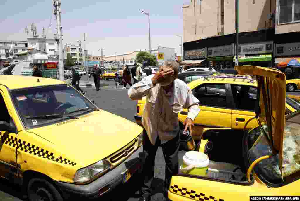 A man in Tehran splashes his face with water from the back of his taxi.  