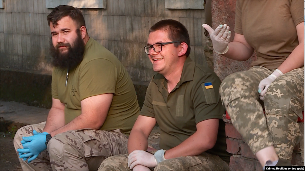 Медики стабпункту під час перепочинку. Південь України, літо 2023 року «Коли ти бачиш, що пацієнта привозять важкого, здавалося б навіть, безнадійного, коли немає шансу на життя, але спільна злагоджена робота усіх нас – коли ми працюємо, як бджоли біля вулика – за 10-15 хвилин командної роботи ми бачимо, що пацієнта вдалося стабілізувати! І вже на таких емоціях, іноді пробиває на сльозу, іноді посмішка на обличчі! Тобто коли ти бачиш такі результати, плоди своєї праці, то це найвища, найкраща оцінка нашої роботи», – каже Денис Нечуя, лейтенант, ординатор лікувального відділення медичної роти 36-тої окремої бригади морської піхоти (на фото в окулярах)  