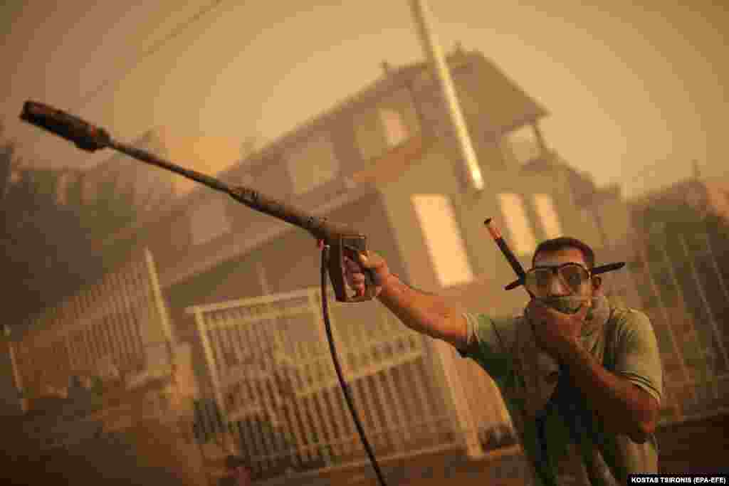Житель в маске для подводного плавания разбрызгивает воду у входа в дом во время лесного пожара в районе Лагониси в Аттике, Греция, 17 июля 2023 года. В результате многочисленных лесных пожаров в Греции 28 человек погибли и 75 получили ранения. (EPA-EFE/KOSTAS TSIRONIS)