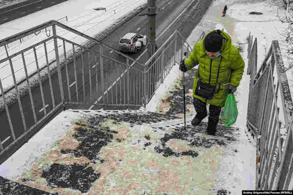 Женщина поднимается по лестнице надземного перехода на улице Комарова. Это единственный способ, позволяющий попасть с остановки внизу в располагающиеся на горе больницу и жилой микрорайон "Танкодром". Подъёмники, на которые были выделены деньги из федерального бюджета по программе "Доступная среда", здесь демонтировали много лет назад. За это время папа мальчика-инвалида Юрий Никишин успел даже выиграть иск к исполкому Казани, в котором он требовал вернуть подъёмники — но чиновники проигнорировали решение суда.