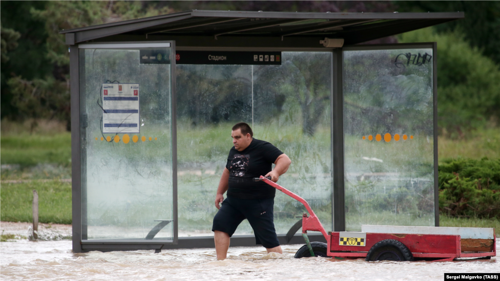 Местный житель на затопленной остановке общественного транспорта. Подконтрольные власти Керчи утверждают, что с утра 14 августа ситуация в городе «остается стабильной»