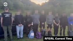 Ukrainians suspected of seeking to cross illegally into Romania stand in line while a Ukrainian border guard (l) faces the other way.