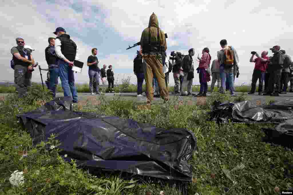 OSCE monitors and journalists look on as a pro-Russian separatist stands guard near bodies taken from a crash site. 