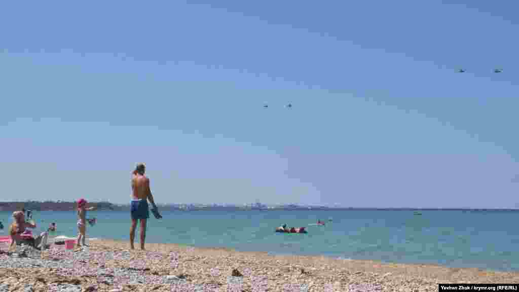 Пляжники спостерігають за російськими військовими гелікоптерами.   (Знімки зроблені незадовго до параду 26 липня, приуроченого до Дня військово-морського флоту в Росії. На фото – гелікоптери повертаються на базу після репетиції)