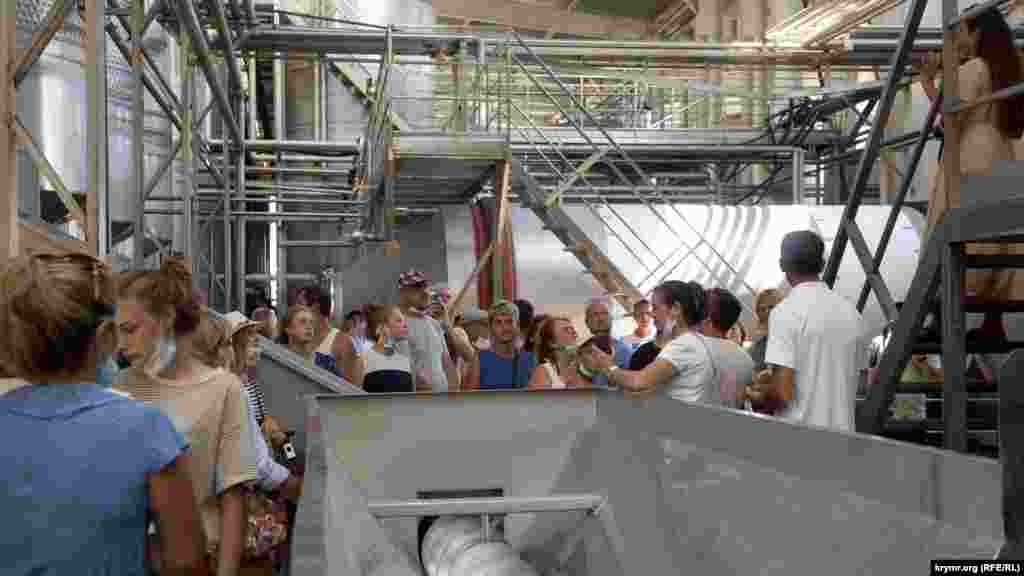 Екскурсійна група на заводі.   Екскурсовод розповідає, як отримують ферментоване (червоне і рожеве) вино. Екскурсія для дорослого обійдеться в 400 рублів (150 грн), для дитини – у 200 рублів (75 грн). Для відвідування закритих цехів обов'язкові маски