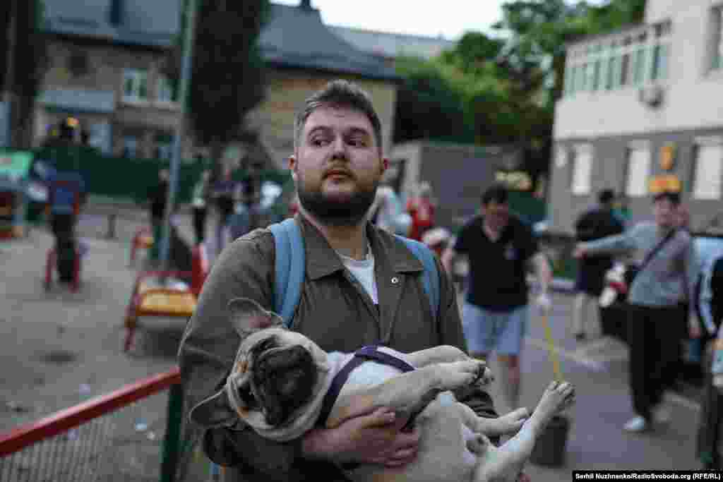 Locuitorii din Kiev au ieșit în fața unei case avariate de un atac aerian rus, în dimineața zilei de 6 iunie 2025.Unul dintre localnici își ține câinele în brațe. Animalele sunt și ele foarte afectate de explozii.
