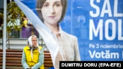 An elderly woman sits on a street bench behind a party campaign tent in downtown Chisinau ahead of a runoff in the presidential election.