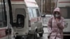 A woman wearing a protective face mask walks past ambulances outside a hospital in Omsk.