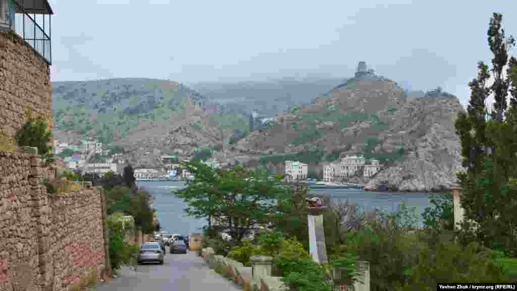 Дорога на пляж «Василі» починається з розташованої на західному узбережжі Балаклавської бухти Таврійської набережної. На протилежному боці видно руїни генуезької фортеці Чембало