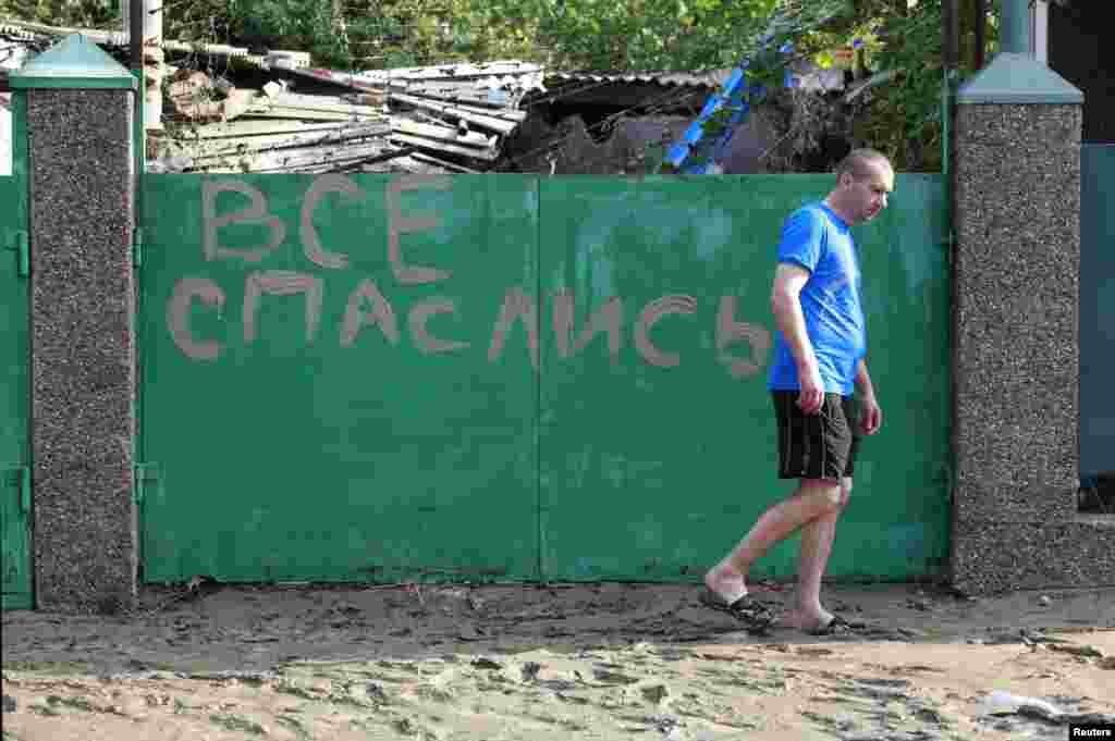 A local resident walks in mud from the floods in the town of Krymsk past a sign reading  "Everyone has escaped (found salvation)."