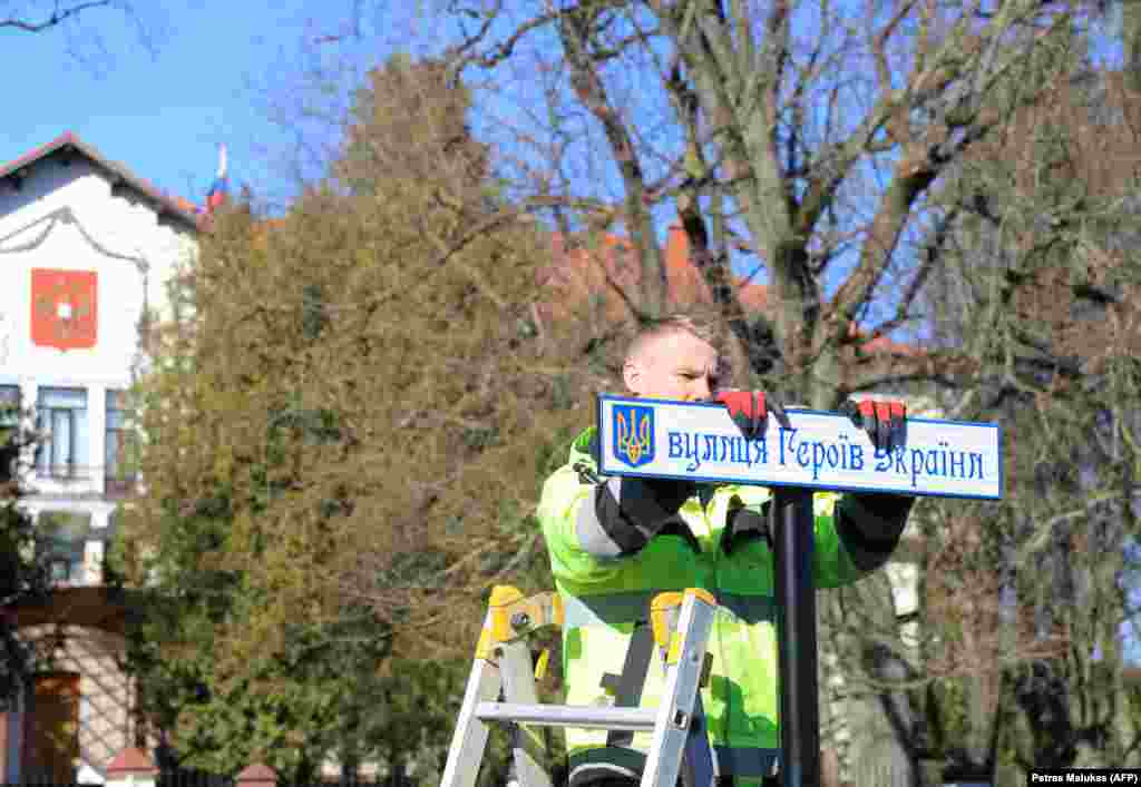 Radnik postavlja uličnu tablu na ukrajinskom jeziku kojom se preimenuje ulica koji vodi do ruske ambasade (vidljiva u pozadini) u Viljnusu, Litvanija, mart 2022. Saobraćajnica se sada zove Ulica ukrajinskih heroja.