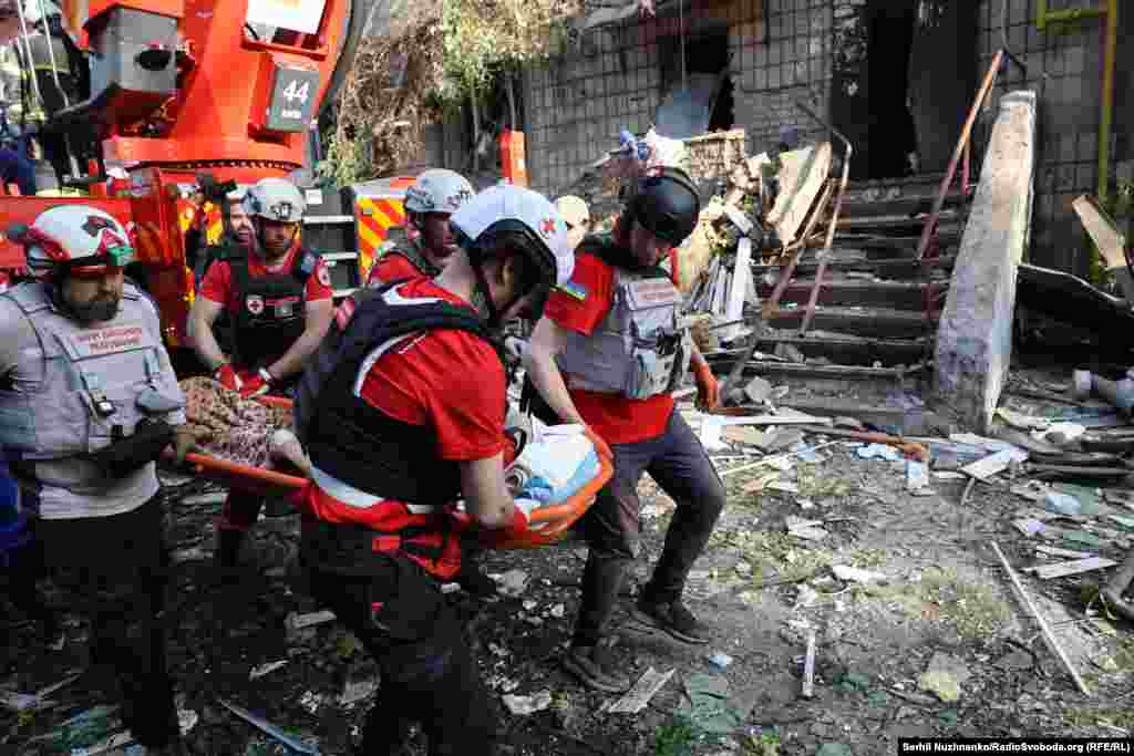 Рятувальники і медики виносять поранену жінку на місці російського удару у житловий будинок. Київ, 17 червня