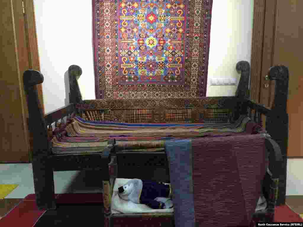 На переднем плане - деревянная колыбель. Сзади - тахта (своего рода диван) и ковер ручной работы