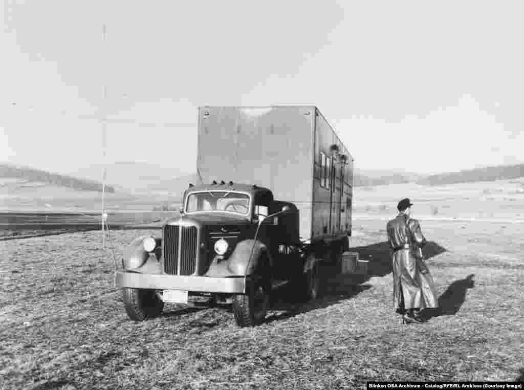 În 1955, un gardian înarmat patrulează lângă un camion cu emițătoare radio pe unde medii în Germania de Vest, în apropierea graniței cu Cehoslovacia.Pe măsură ce statele comuniste încercau să bruieze emisiunile RFE și Radio Liberty, Radio Europa Liberă a desfășurat zeci de stații de emisie mobile, precum cea de mai sus, care puteau funcționa în apropierea Cortinei de Fier.