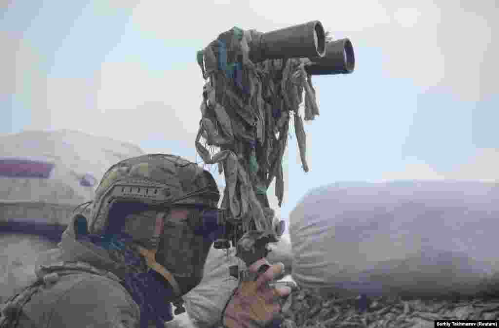 Український військовий дивиться в бінокль під час спостереження за бойовими позиціями російських гібридних сил на лінії розмежування поблизу окупованого Донецька, 6 квітня