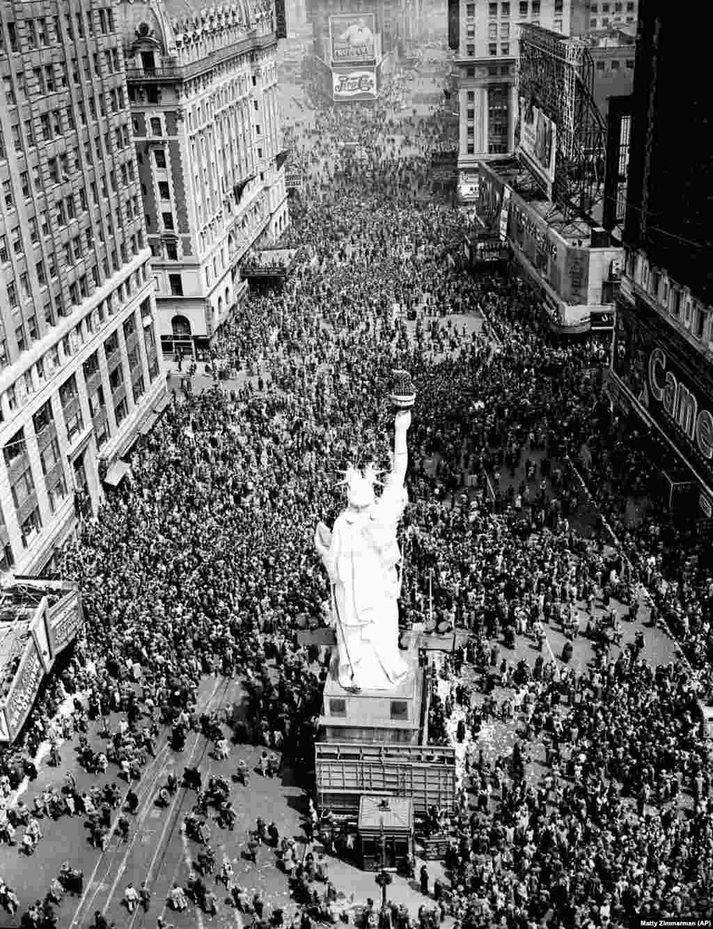 New York City, Statele Unite ale Americii, 8 mai 1945 - Oamenii se înghesuie în Times Square, jurul unei copii a Statuii Libertății. Un reporter descrie scena: „Ici și colo, un civil amețit, uneori un militar, oferă băuturi străinilor. Băuturile sunt acceptate cu ușurință, mai ales de către adolescenți”.