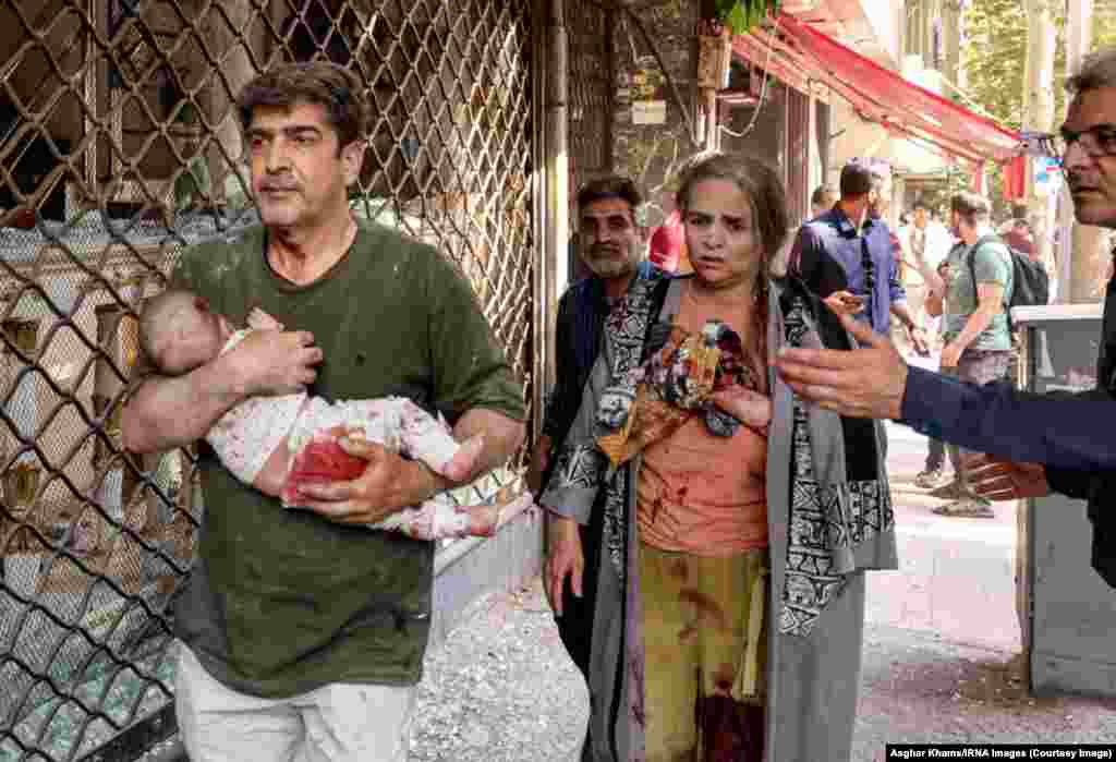 Iran, 15 iunie 2025. Un bărbat duce în brațe un bebeluș, după o lovitură israeliană la Teheran.