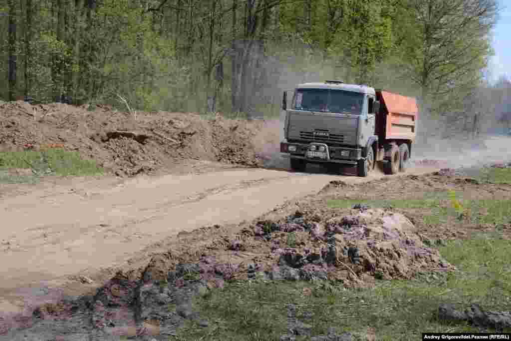 КАМАЗ свозит грунт, снятый с дороги, на лужайку. 