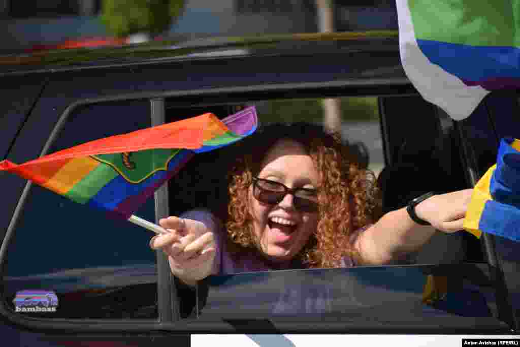 Учасниця під час руху колони махає через відкрите вікно автівки веселковим прапорцем, вітаючи харків’ян.Під час руху маршрутом учасники пробігу також вітали містян автомобільними сигналами