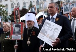 Митрополит Сімферопольський і Кримський УПЦ (МП) Лазар (посередині) і керівник окупованого Росією Криму Сергій Аксьонов (праворуч) під час акції пам’яті «Безсмертний полк». Окупований Сімферополь, 9 травня 2017 року