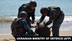 Ukrainian soldiers defuse an anti-ship mine thrown ashore by a storm in 2022.
