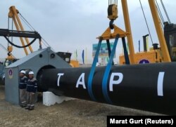 Turkmen workers stand near a gas pipe during the February 23 launching ceremony for construction work on the TAPI pipeline.