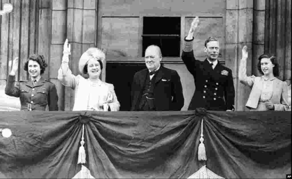 Londra, Marea Britanie, 8 mai 1945 - Prim-ministrul britanic Winston Churchill, în balconul Palatului Buckingham, alături de familia regală, în aplauzele mulțimii. În acea seară, viitoarea regină Elisabeta a II-a (stânga) și prințesa Margaret (dreapta) se strecoară prin mulțime pentru a se alătura petrecerii. Elizabeth a descris experiența ca fiind „una dintre cele mai memorabile nopți din viața mea”.