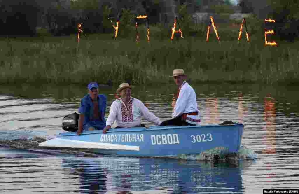 Люди в човні під час свята. Позаду них на березі – напис із палаючих букв «Купалле»