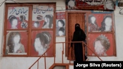 A woman wearing a niqab enters a beauty salon where the ads of women have been defaced by a shopkeeper in Kabul.