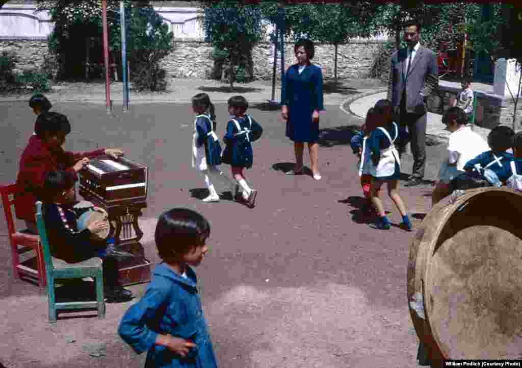 Young Afghan students dance on a school playground as a teacher and a student accompany on instruments.