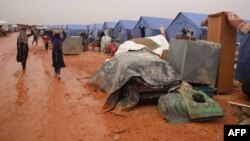Women carry water in a camp for displaced Syrians on the outskirts of the northwestern city of Maaret Misrin near the Turkish border, on February 6, 2020.