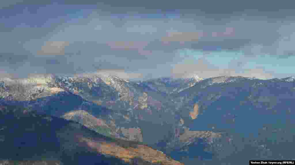 Вершини гір в снігу, темні хмари і блакитне небо в просвітах – картина, гідна художника