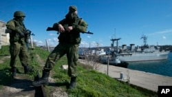 Soldați ruși („omuleții verzi”) păzesc un debarcader cu două nave militare ucrainene în fundal, la Sevastopol, în Peninsula Crimeea, pe 5 martie 2014.