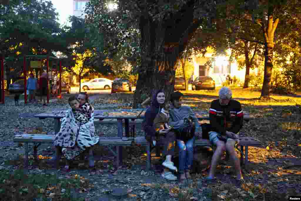 Люди сидять біля пошкодженого будинку